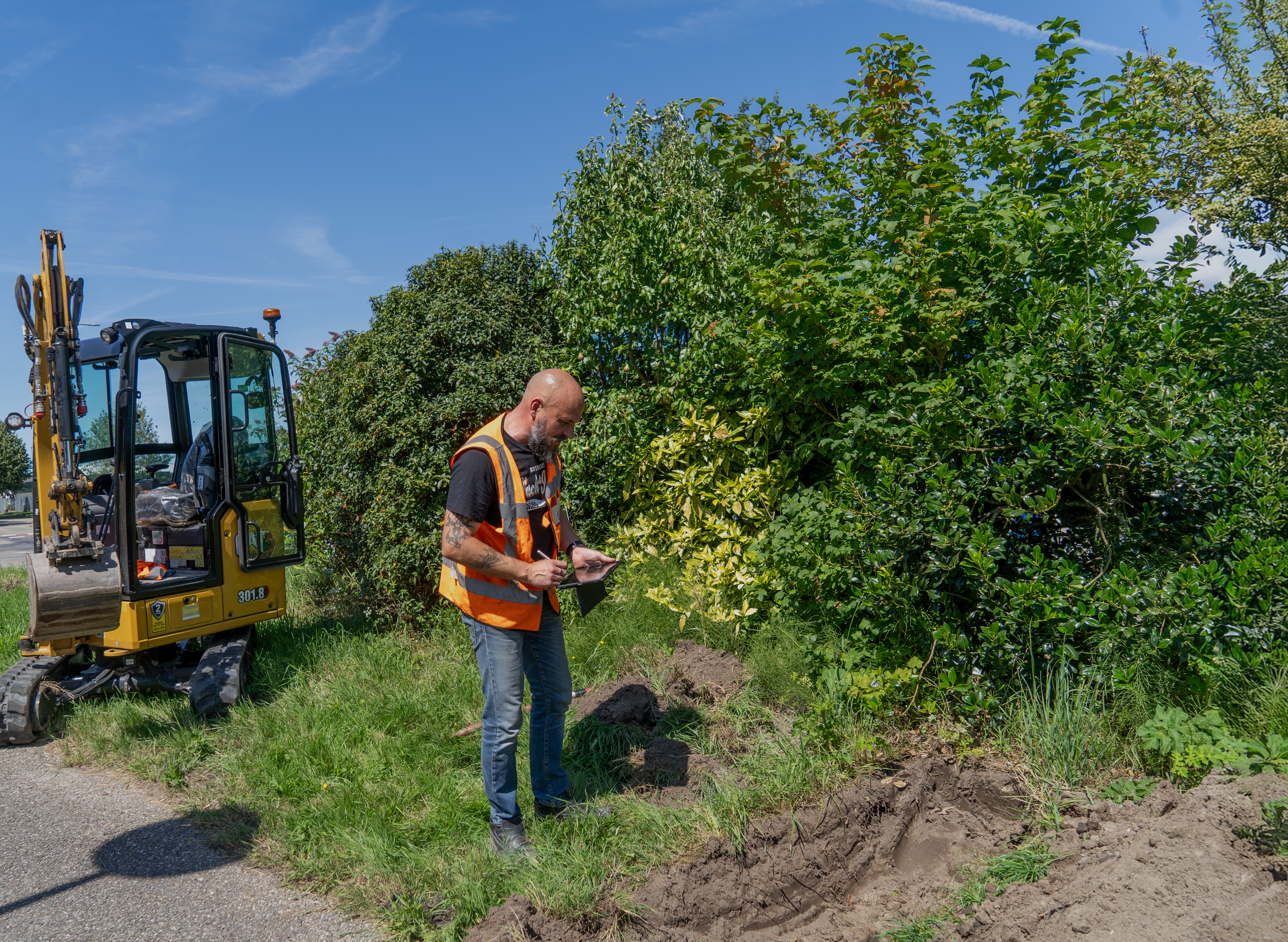 Professional using Proefsleuf App on tablet at construction site with excavator
